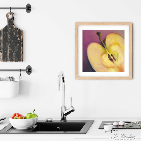 A square apple painting art print in a simple, elegant wood frame on a kitchen wall. Placed above a modern sink, with rustic chopping boards and fresh vegetables.