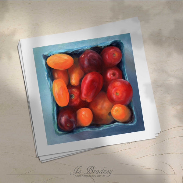 A stack of square art prints on archival paper on a wood kitchen counter. The prints show a box of heirloom cherry tomatoes. This is a giclee print of my realistic oil painting still life. The original artwork is sold.