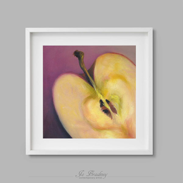 A cream and yellow apple, cut in half on a soft rose-pink background. A warm heart at the core of the fruit. This square archival art print of my apple still life oil painting is shown in simple white picture frame.