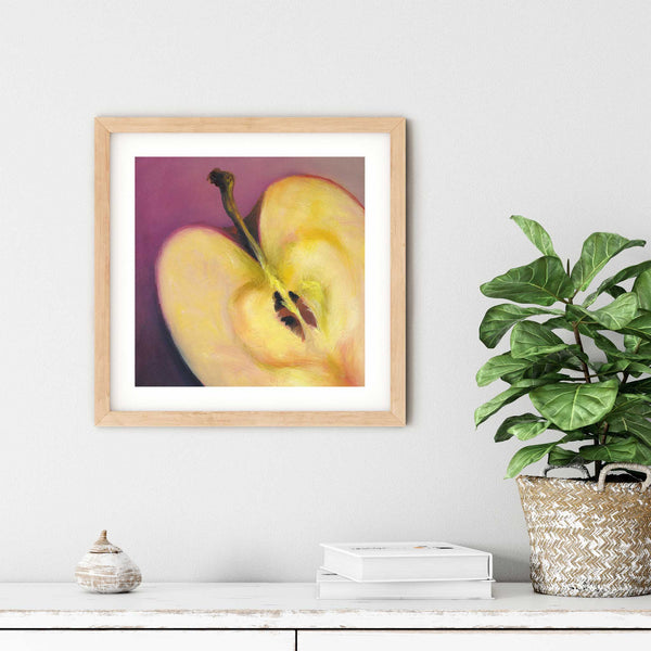 A pink and cream apple oil painting art print in a simple elegant wood frame on a dining room or living room wall. There are books and a plant in a rustic pot, on a shabby chic painted wood buffet table.