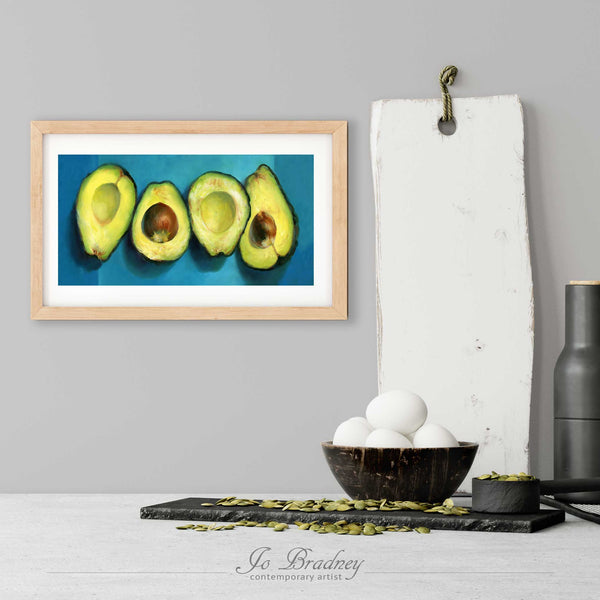 A skinny avocado art print in a simple, elegant wood picture frame on a kitchen wall. There is a bowl of eggs, and a chopping board for scale. The print is 5 eggs tall. The smallest long narrow panoramic print is 4x8 inches, the largest is 10x20 inches.