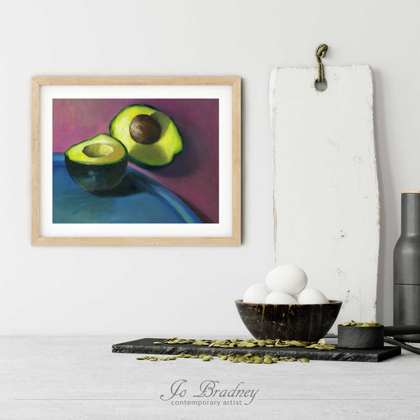 An avocado art print in a simple, elegant wood picture frame on a kitchen wall. There is a bowl of eggs, and a chopping board for scale. The print is 5 eggs tall. The smallest horizontal print is 4x6 inches, the largest is 11x14 inches.