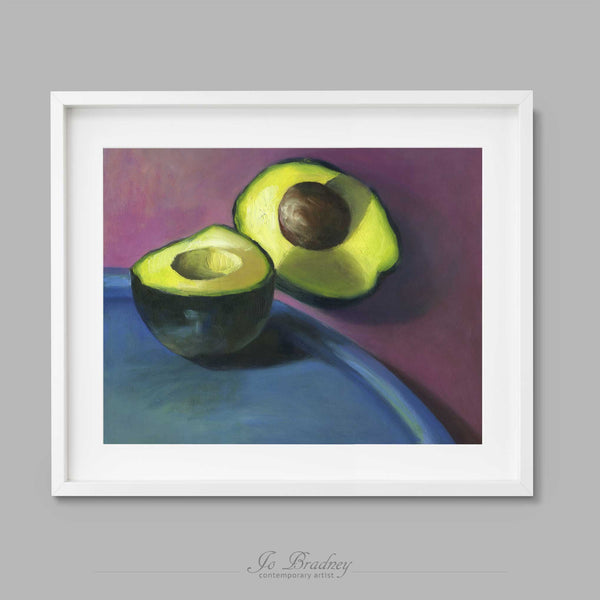Bright green avocado on a purpleand teal blue background. This archival art print of my vegetable still life oil painting is shown in simple white picture frame.
