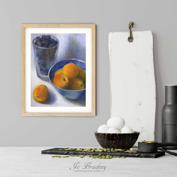 An apricot and blueberry art print in a simple, elegant wood picture frame on a kitchen wall. There is a bowl of eggs, and a chopping board for scale. The print is 5 eggs tall. The smallest vertical print is 4x6 inches, the largest is 11x14 inches.