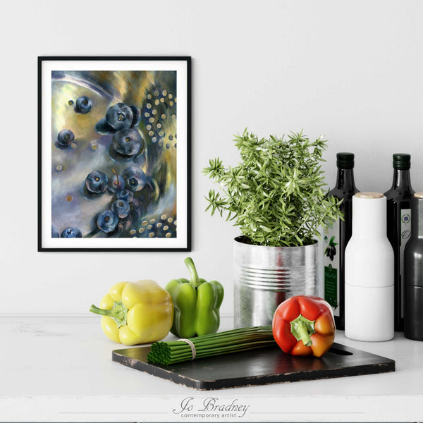 A blueberry painting print in a simple, elegant black picture frame on a kitchen wall. There is a chopping board, vegetables, herbs and some bottles. The art print is as large as three bell peppers. The largest size is 14 inches high by 11 wide