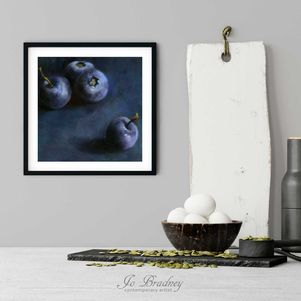 A blueberry art print in a simple, elegant black picture frame on a kitchen wall. There is a bowl of eggs, and a chopping board for scale. The print is 5 eggs tall. The smallest square print is 4 inches, the largest is 12 inches.