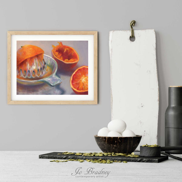 An art print of oranges in a simple, elegant wood picture frame on a kitchen wall. There is a bowl of eggs, and a chopping board for scale. The print is 5 eggs tall. The smallest horizontal print is 4x6 inches, the largest is 11x14 inches.