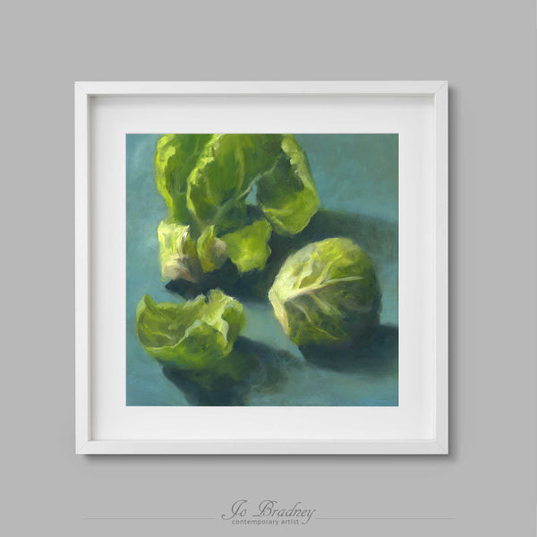 A fresh green Brussels Sprout on a teal green background. This archival art print of my vegetable still life oil painting is shown in simple white picture frame.