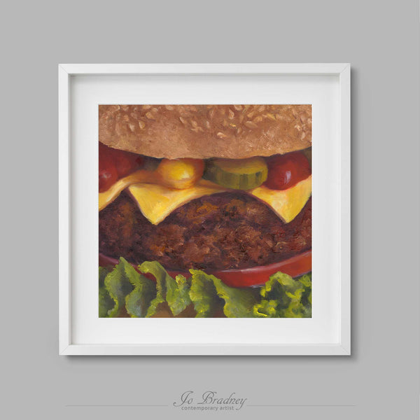 A close up of a burger in a bun, with melted cheese, pickle, ketchup and mustard. The tomato slice makes a smile. This archival art print of my [SUBJECT] still life oil painting is shown in simple white picture frame.
