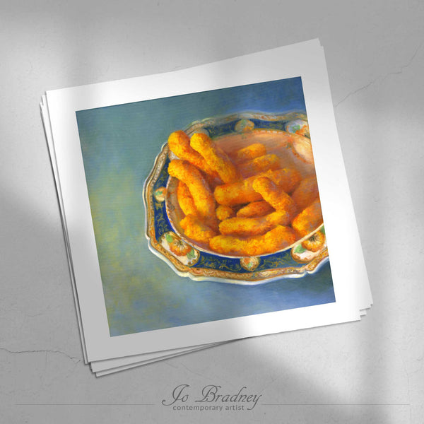 A stack of square art prints on archival paper on a stone kitchen counter. The prints show a fancy porcelain bowl filled with Cheetos cheese puffs. This is a giclee print of my realistic oil painting still life. The original artwork is sold.