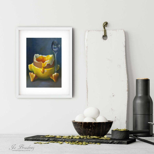 A funny breakfast egg art print in a simple, elegant white picture frame on a kitchen wall. There is a bowl of eggs, and a chopping board for scale. The print is 5 eggs tall. The smallest vertical art print is 4x6 inches, the largest is 11x14 inches.
