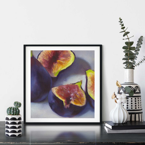 A fig oil painting fruit art print framed in a simple, elegant black picture frame on a dining room or living room wall. There are flowers in vase, set on a wood buffet table. The smallest square print on paper is 4 inches, the largest is 12 inches.