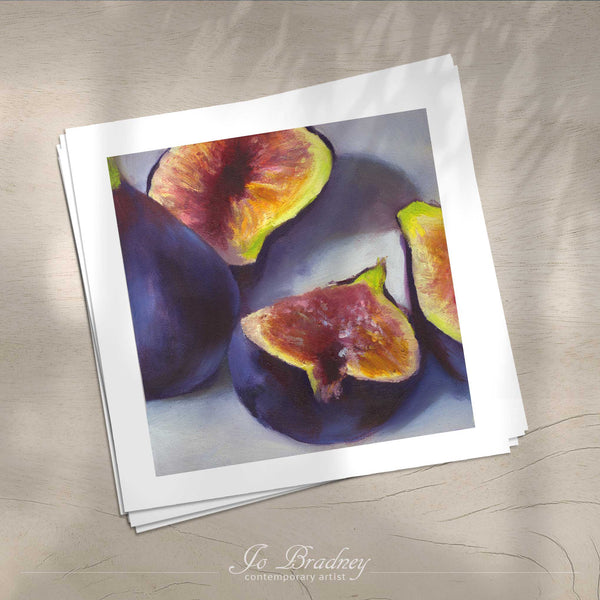 A stack of square art prints on archival paper on a wood kitchen counter. The prints show a fresh purple fig, cut to show the pink fruit inside. This is a giclee print of my realistic oil painting still life. The original artwork is sold.