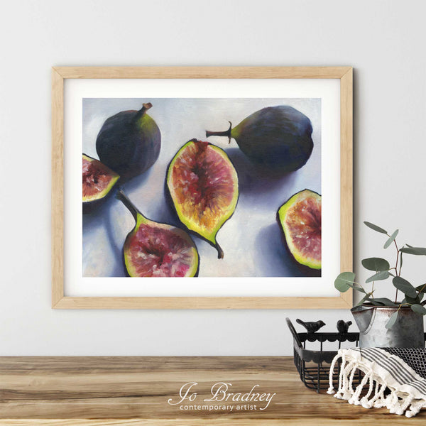 A fresh fig art print in a simple, elegant wood picture frame on a dining room or living room wall. There are flowers in a teapot on a metal tray set on a wood table. The smallest horizontal print is 4x6 inches, the largest is 11x14 inches.