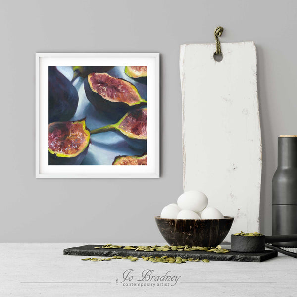 A modern fruit art print of Mission figs in a simple, elegant white picture frame on a kitchen wall. There is a bowl of eggs, and a chopping board for scale. The print is 5 eggs tall. The smallest square print is 4 inches, the largest is 12 inches.