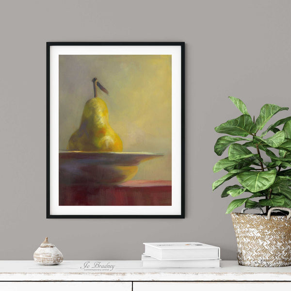 A gold fall pear oil painting print in a simple elegant black frame on a dining room or living room wall. There are books and a plant in a rustic pot, on a shabby chic painted wood buffet table.