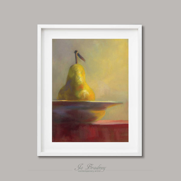 A gold pear in a white china bowl on a red table, against a sage green wall. This archival art print of my fruit still life oil painting is shown in simple white picture frame.