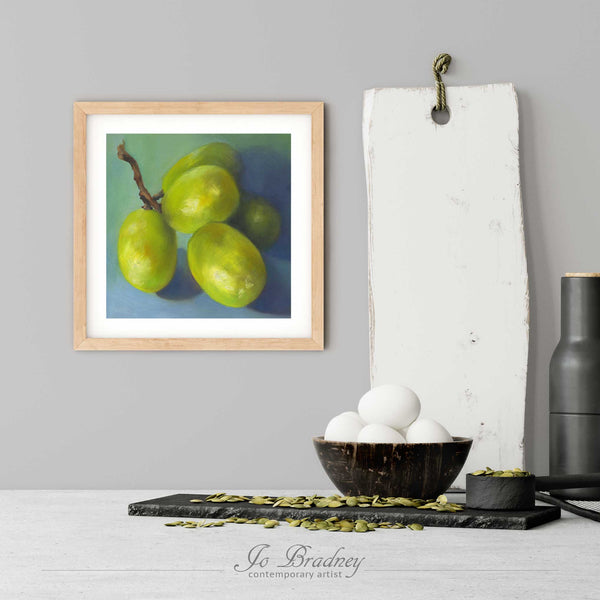 A modern grapes still life art print in a simple, elegant wood picture frame on a kitchen wall. There is a bowl of eggs, and a chopping board for scale. The print is 5 eggs tall. The smallest square print is 4 inches, the largest is 12 inches.