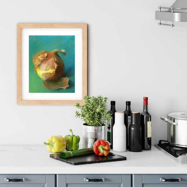 A colorful green and yellow onion painting art print in a simple, elegant wood picture frame on a kitchen wall. There is a chopping board, vegetables, herbs and some bottles. The art print is as large as three bell peppers. The largest size is 14 inches high by 11 wide