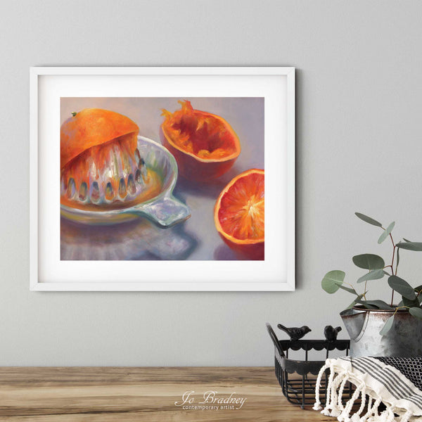 A orange juice art print in a simple, elegant white picture frame on a dining room or living room wall. There are flowers in a teapot on a metal tray set on a wood table. The smallest horizontal print is 4x6 inches, the largest is 11x14 inches.