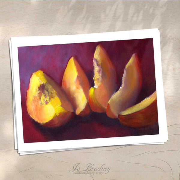 A stack of horizontal giclee fine art prints on archival paper on a wood kitchen counter. The prints show a sliced peach on a purple red background. This is a giclee print of my realistic oil painting still life. The original artwork is sold.