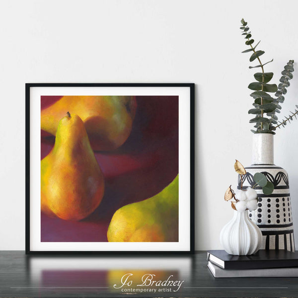 A golden pear oil painting art print framed in a simple, elegant black picture frame on a dining room or living room wall. There are flowers in vase, set on a wood buffet table. The smallest square print on paper is 4 inches, the largest is 12 inches.