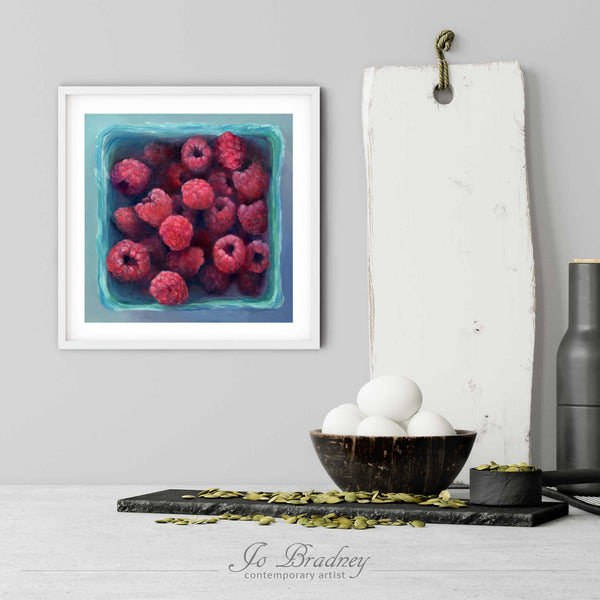 A pink and green raspberry art print in a simple, elegant white picture frame on a kitchen wall. There is a bowl of eggs, and a chopping board for scale. The print is 5 eggs tall. The smallest square print is 4 inches, the largest is 12 inches.