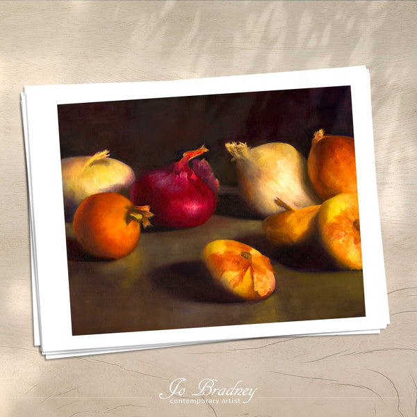 A stack of horizontal art prints on archival paper on a wood kitchen counter. The prints show red, yellow, brown and white onions on a dark background. This is a giclee print of my realistic oil painting vegetable still life. The original artwork is sold.