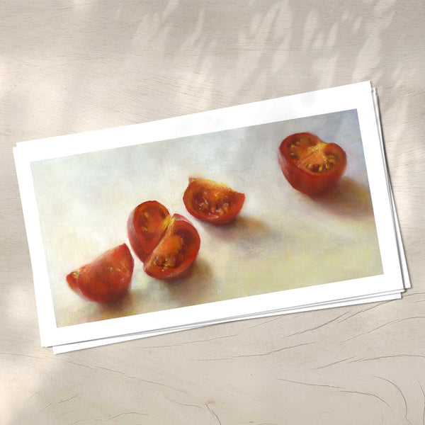 A stack of red tomato art prints on archival paper on a wood kitchen counter. The prints show fresh chopped tomato on a white background. This is a giclee print of my realistic oil painting still life. The original artwork is sold.
