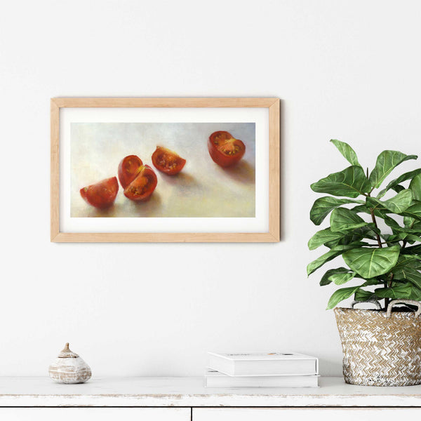 A frsh tomato oil painting art print in a simple elegant wood frame on a dining room or living room wall. There are books and a plant in a rustic pot, on a shabby chic painted wood buffet table.