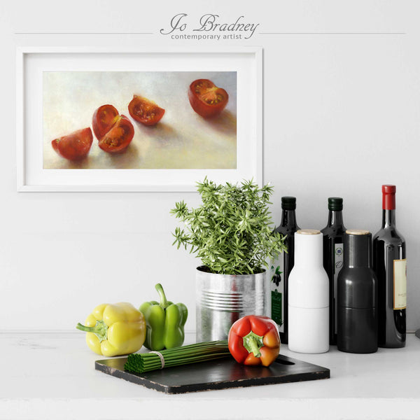 A red tomato painting art print in a simple, elegant white picture frame on a kitchen wall. There is a chopping board, vegetables, herbs and some bottles. The art print is as long as four bell peppers. The largest size is 10 inches high by 20 wide