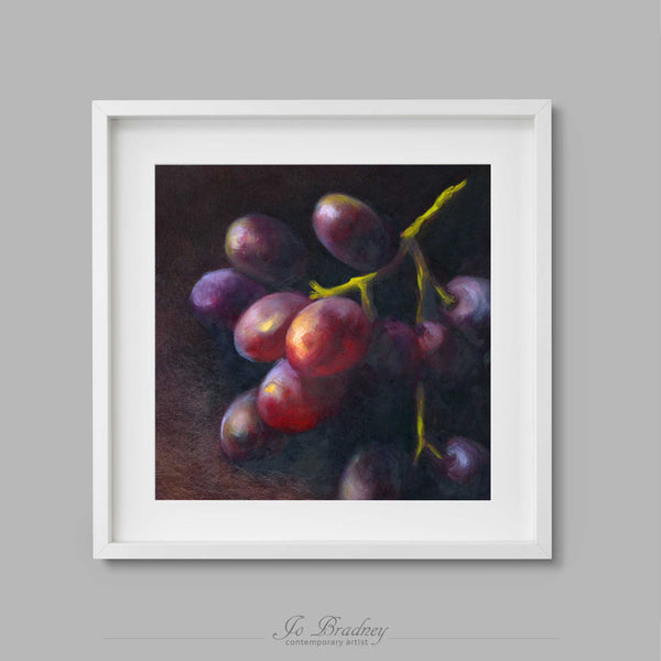 Rich purple and red grapes emerge from a dark background.. This archival art print of my fruit still life oil painting is shown in simple white picture frame.